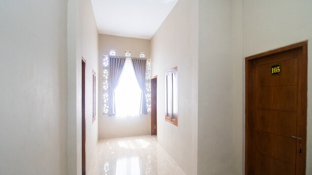A hallway with a wooden door marked 105, a window with curtains, and a light-colored floor. - RedDoorz Syariah near UNTAG Banyuwangi 2 (Banyuwangi)