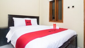 A neatly made bed with white and red bedding, a wooden headboard, and a window with wooden blinds. - RedDoorz Syariah near UNTAG Banyuwangi 2 (Banyuwangi)