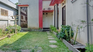 A courtyard with a pathway, a small garden, and a building with a red and white facade. - RedDoorz near Paralayang Batu (Batu)