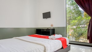 A hotel room with a bed, a TV mounted on the wall, and a window with curtains. - RedDoorz near Paralayang Batu (Batu)