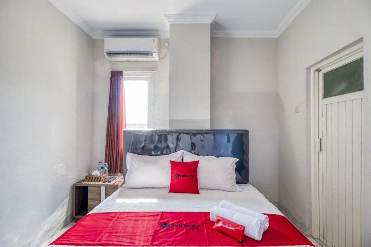 Habitación de hotel con cama, mesita de noche, aire acondicionado, ventana con cortinas y puerta.
