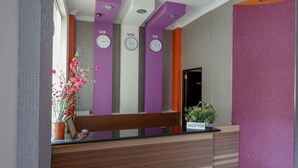 Un comptoir d’accueil avec un banc en bois, une plante en pot et trois horloges sur des murs violets.