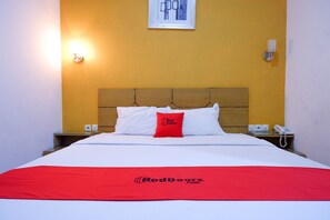 Una habitación de hotel con cama, mesita de noche y lámpara de pared.