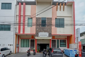A hotel with a signboard, a parking area with cars and motorcycles, and a building facade with red and beige colors.