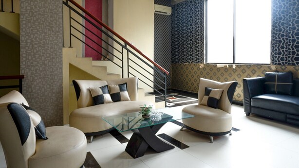 Un salon avec une table basse en verre, deux canapés, un escalier et un papier peint à motifs.
