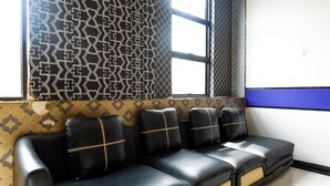 Un canapé en cuir noir agrémenté de touches de jaune, placé devant un mur à motifs et près d’une grande fenêtre.