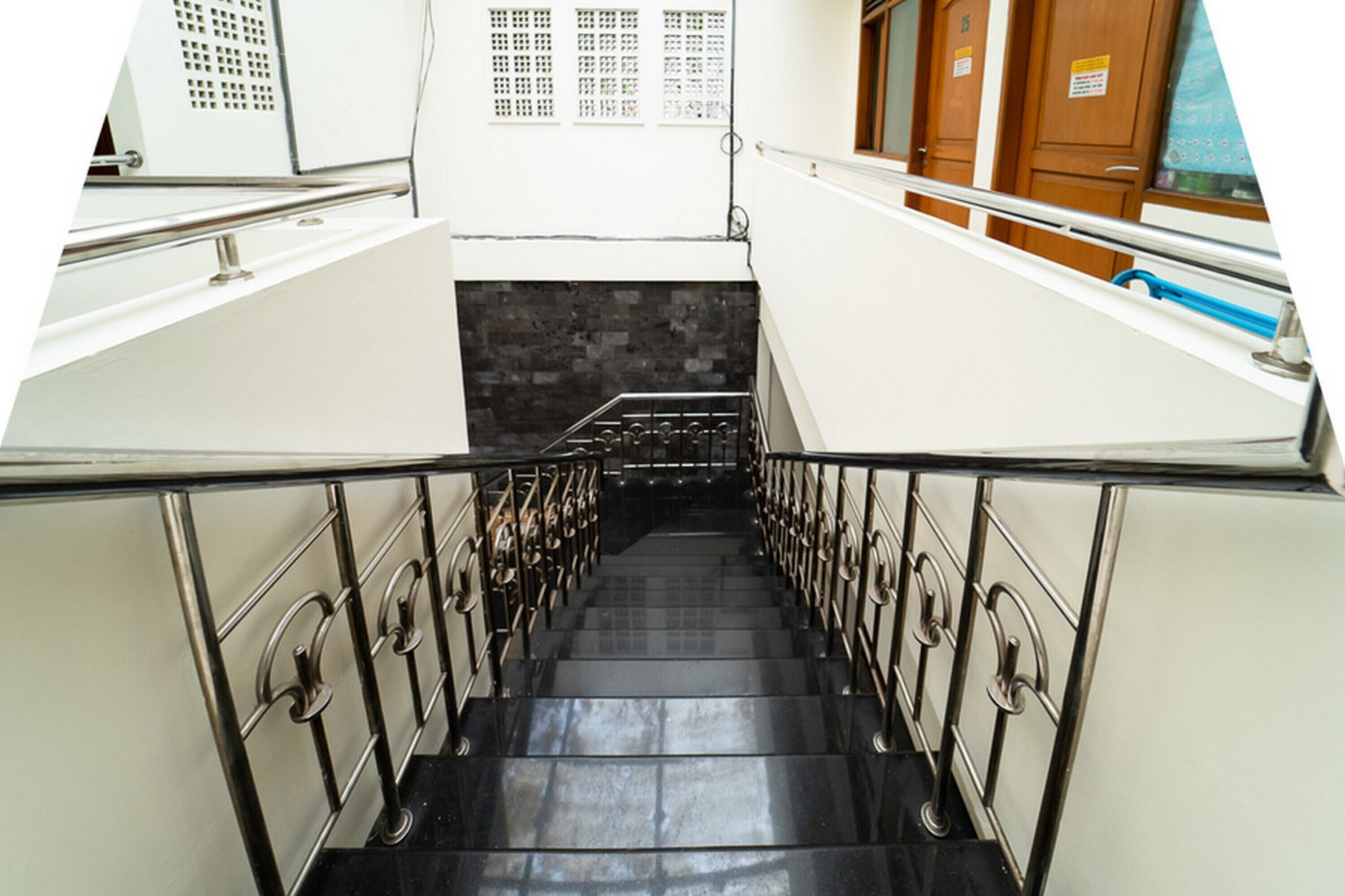 Eine Treppe mit Metallgeländern, einem schwarzen Fliesenboden und einer weißen Wand mit Fenster und Tür.