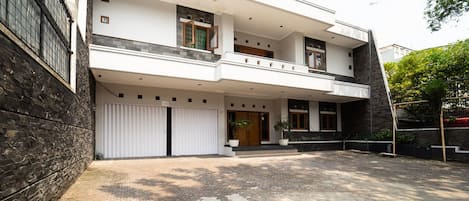A modern two-story house with a spacious driveway, a balcony on the upper floor, and a large garage door.