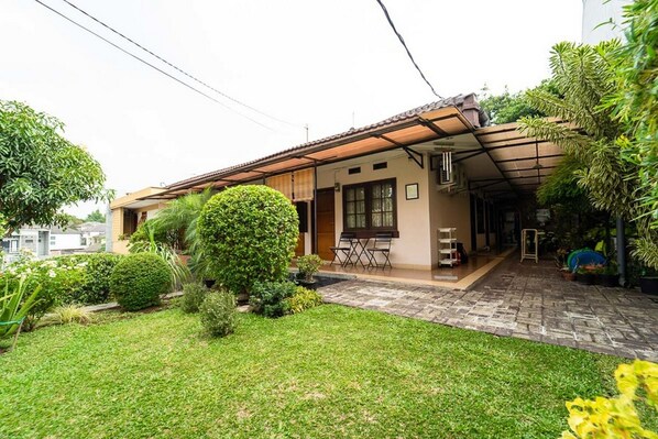 Einbungalow mit einer gefliesten Terrasse, einem kleinen Garten mit verschiedenen Pflanzen und einem überdachten Sitzbereich.