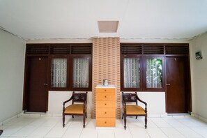Ein Zimmer mit zwei hölzernen Stühlen, einem zentralen Holzschrank und zwei großen Fenstern mit Holzläden.