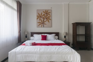 Cama bem arrumada com roupa de cama branca e detalhes vermelhos, cabeceira de madeira e uma obra de arte na parede com folhas.
