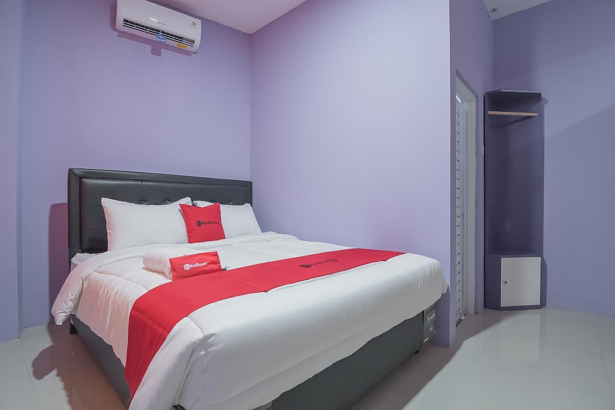 Una cama bien tendida con ropa de cama blanca y roja, un cabecero negro y una almohada roja con un logo.