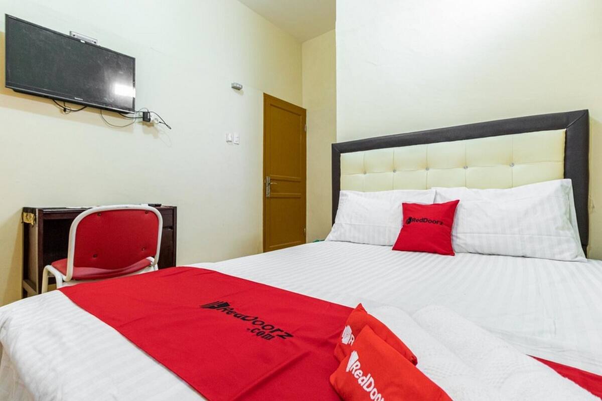 A hotel room with a bed, a desk, a chair, and a television on the wall.