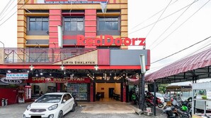 A building with a red and yellow facade, a sign for 'Surya Swalayan' at the top, and a covered area with motorcycles parked outside. - RedDoorz Syariah @ Jalan Setiabudi Medan 3 (Medan)