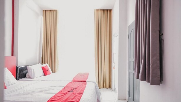A hotel room with a bed, curtains, and a door. - RedDoorz @ Jalan Sukabangun 2 Palembang (Palembang)