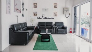 A modern living room with black leather sofas, a central coffee table, and a green rug. - RedDoorz @ Jalan Sukabangun 2 Palembang (Palembang)