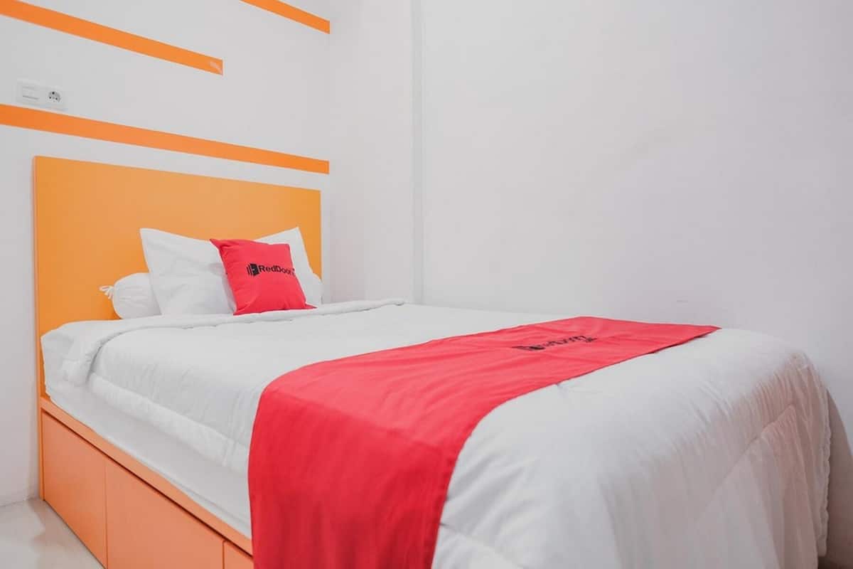 Un lit avec une tête de lit orange, du linge de lit blanc et une couverture rouge.