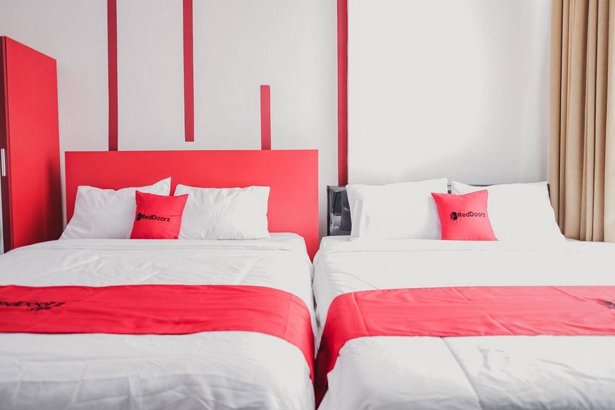 Une chambre d’hôtel avec deux lits, chacun agrémenté de linge de lit blanc et de touches de couleur rouge, notamment au niveau des oreillers et des têtes de lit.