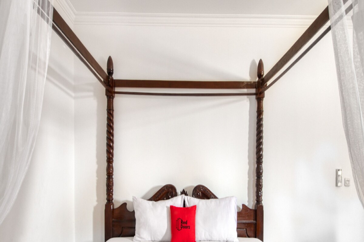 Una cama con dosel con ropa de cama blanca y roja, un cojín rojo con texto y una manta roja con texto.
