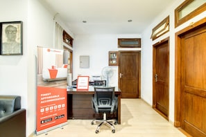 Zona de recepción con escritorio, una silla, un ventilador y una puerta de madera.