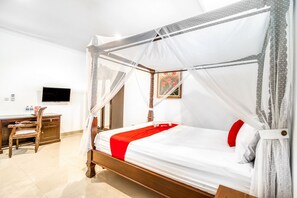 A four-poster bed with a canopy, a wooden desk with a chair, and a flat-screen TV on the wall. - RedDoorz Plus near Lempuyangan Station 4 (Yogyakarta)