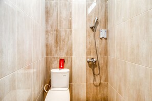 Baño con azulejos color beige, un inodoro, ducha con cabezal de ducha manual y dispensador de toallas rojo.