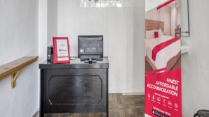 Un mostrador de recepción de hotel con un letrero de RedDoorz, una pantalla digital y un cartel promocional de alojamiento.