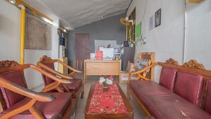 A reception area with a reception desk, wooden chairs, a red sofa, and a table with a floral tablecloth. - RedDoorz @ Jalan Cilik Riwut Kapuas (Kualakapuas)