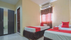 A hotel room with two beds, each with a red and white bedspread, and a red pillow with the hotel's logo. There is a wardrobe, a window with curtains, and an air conditioning unit above the window. - RedDoorz @ Jalan Cilik Riwut Kapuas (Kualakapuas)