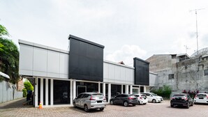 Un estacionamiento con varios coches aparcados frente a un edificio de grandes ventanales y techo plano.