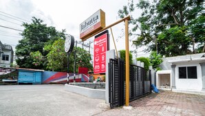 Una entrada protegida por un portón a una propiedad, con un letrero que dice 'Jabutta Guesthouse' y un cartel de RedDoorz que indica servicios como Wi-Fi, estacionamiento y restaurante.