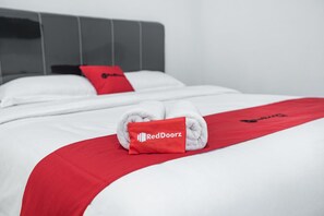 Ein ordentlich bezogenes Bett mit weißen Leinen und einer roten Decke, verziert mit dem RedDoorz-Logo.