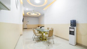 Un salón de conferencias con una mesa de vidrio, sillas color crema, un dispensador de agua y un techo con luminarias circulares.