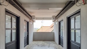 A corridor with two doors leading to a balcony with a view of a red-tiled roof. - RedDoorz Syariah near Galeria Mall Yogyakarta (Yogyakarta)