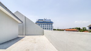 A rooftop terrace with a concrete floor and low walls, overlooking a building with multiple windows and a blue roof. - RedDoorz Syariah near Galeria Mall Yogyakarta (Yogyakarta)