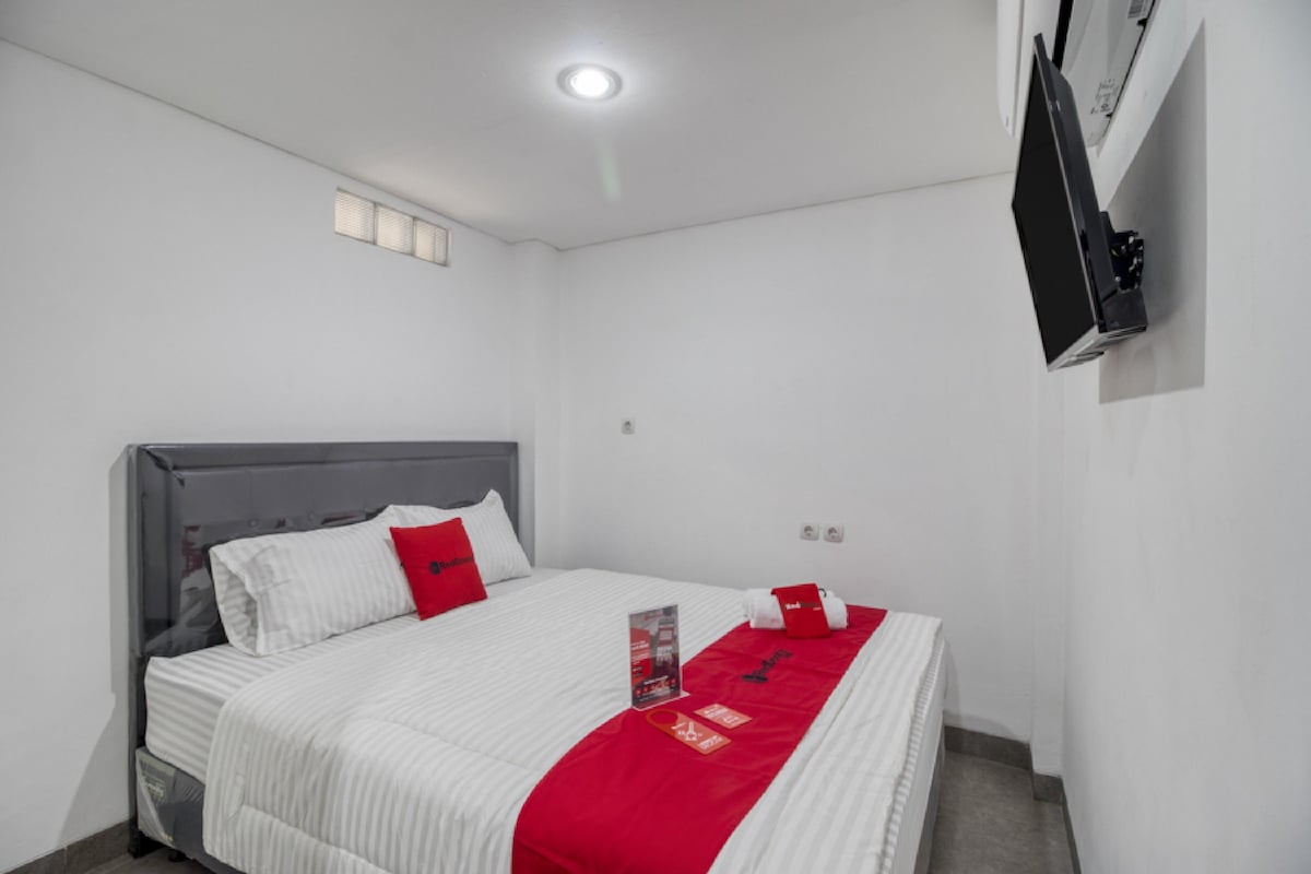 A hotel room with a bed, a flat-screen TV mounted on the wall, and a ceiling light.