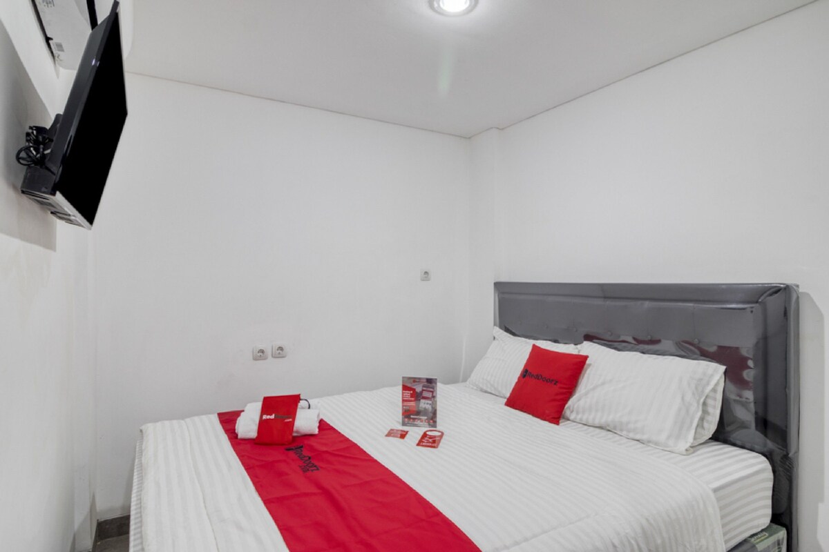 Habitación de hotel con cama, televisor de pantalla plana montado en la pared y una colcha de color rojo y blanco.