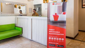 A reception area with a green sofa, a reception desk, and a RedDoorz advertisement. - RedDoorz near Alun Alun Bandung 2 (Bandung)
