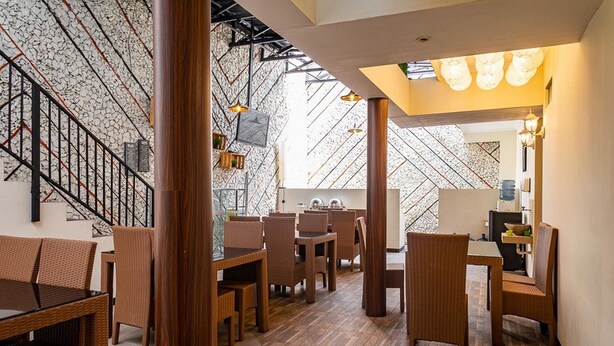 A restaurant with wicker furniture, a staircase with a patterned wall, and a ceiling with hanging lights. - RedDoorz near Alun Alun Bandung 2 (Bandung)