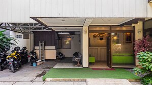 A building with a covered parking area, a green artificial lawn, and a few chairs outside. - RedDoorz near Alun Alun Bandung 2 (Bandung)