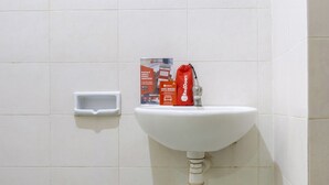 A white sink with a red bag and a soap dispenser on the wall. - RedDoorz near Widya Mandala University (Surabaya)