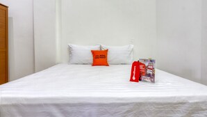 A single bed with white bedding and an orange pillow. A red object, possibly a bag or accessory, is placed on the bed. - RedDoorz near Widya Mandala University (Surabaya)