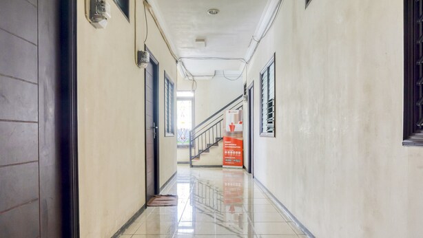 A clean, well-lit hallway with a tiled floor, a staircase at the end, and a fire safety sign. - RedDoorz near Widya Mandala University (Surabaya)