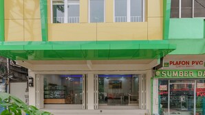 A building with a green and yellow facade, a storefront with signage for 'PLAFON PVC' and 'SUMBER DA', and a glass door entrance. - RedDoorz Plus near RS RK Charitas 2 Palembang (Palembang)