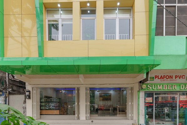 A building with a green and yellow facade, a storefront with signage for 'PLAFON PVC' and 'SUMBER DA', and a glass door entrance.