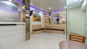 A modern reception area with a reception desk, seating, a painting, and a glass partition. - RedDoorz Plus near RS RK Charitas 2 Palembang (Palembang)