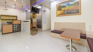 A modern hotel lobby with a reception desk, a flat-screen TV, a painting of a landscape, and a seating area with a table and benches. - RedDoorz Plus near RS RK Charitas 2 Palembang (Palembang)