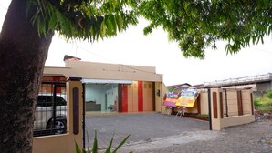 A building with a gated entrance, a paved driveway, and a small garden area with a tree and plants. - RedDoorz near GOR Satria 3 (Purwokerto)