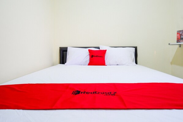 Un lit avec une literie blanche et une couverture rouge ornée du logo RedDoorz.