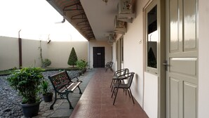 A covered outdoor corridor with a bench, chairs, potted plants, and a door. - RedDoorz near GOR Satria 3 (Purwokerto)